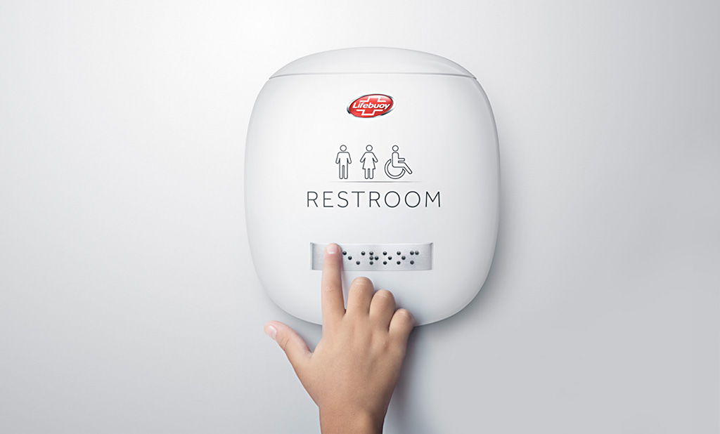 A child's finger gliding across a Clean Braille restroom sign.